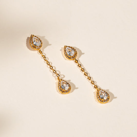 Gold teardrop earrings with clear gemstones on a beige background