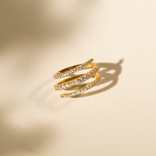 Gold spiral ring with embedded stones on a beige background
