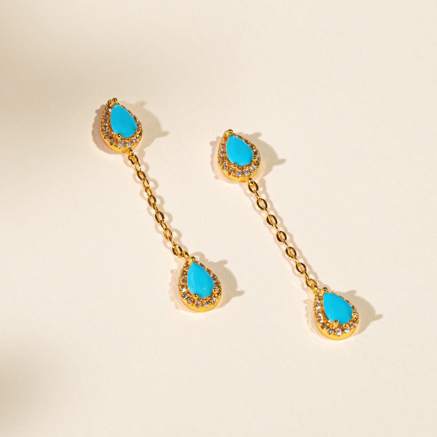 Pair of gold earrings with turquoise stones on a beige background