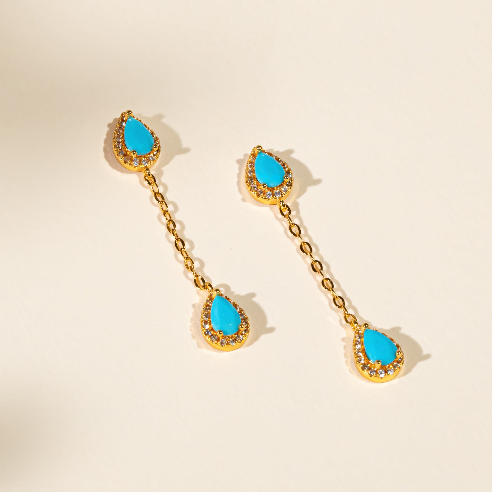 Pair of gold earrings with turquoise stones on a beige background