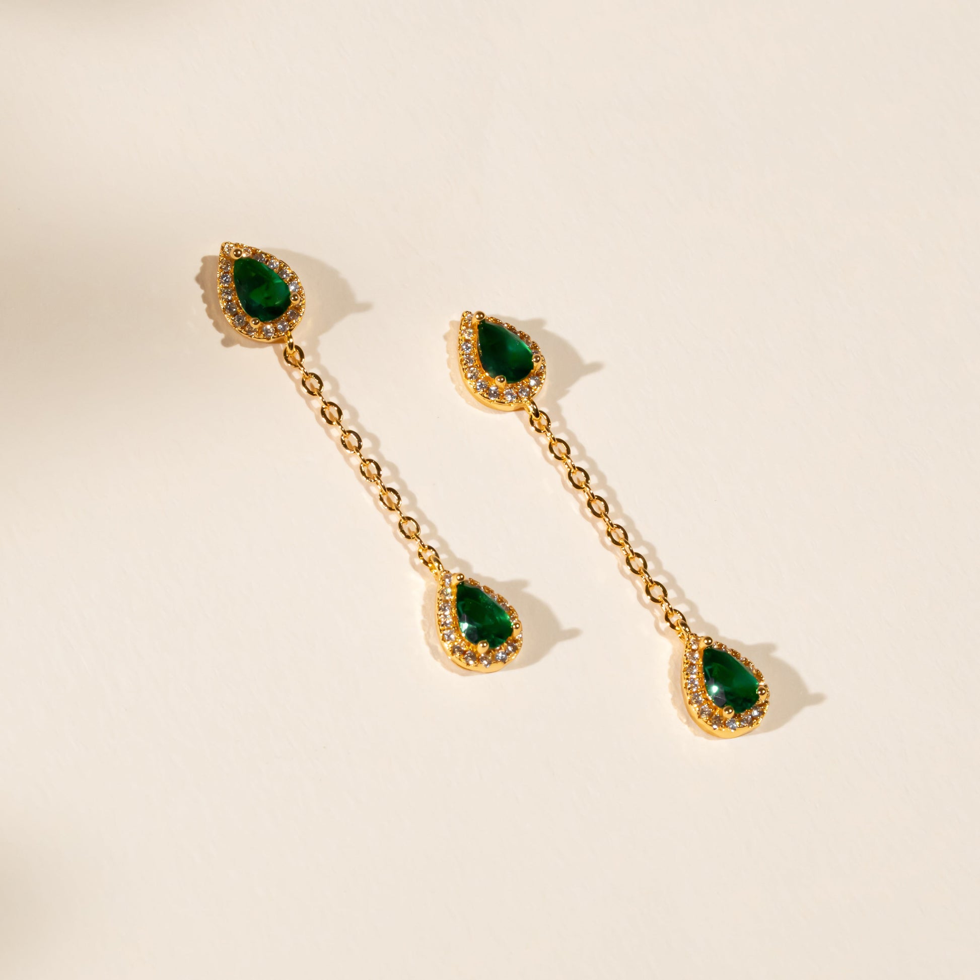 Gold earrings with green gemstones on a beige background
